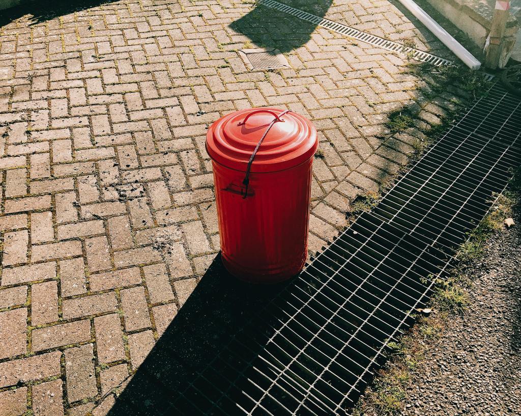Red bucket placed near a storm drain on a paved surface